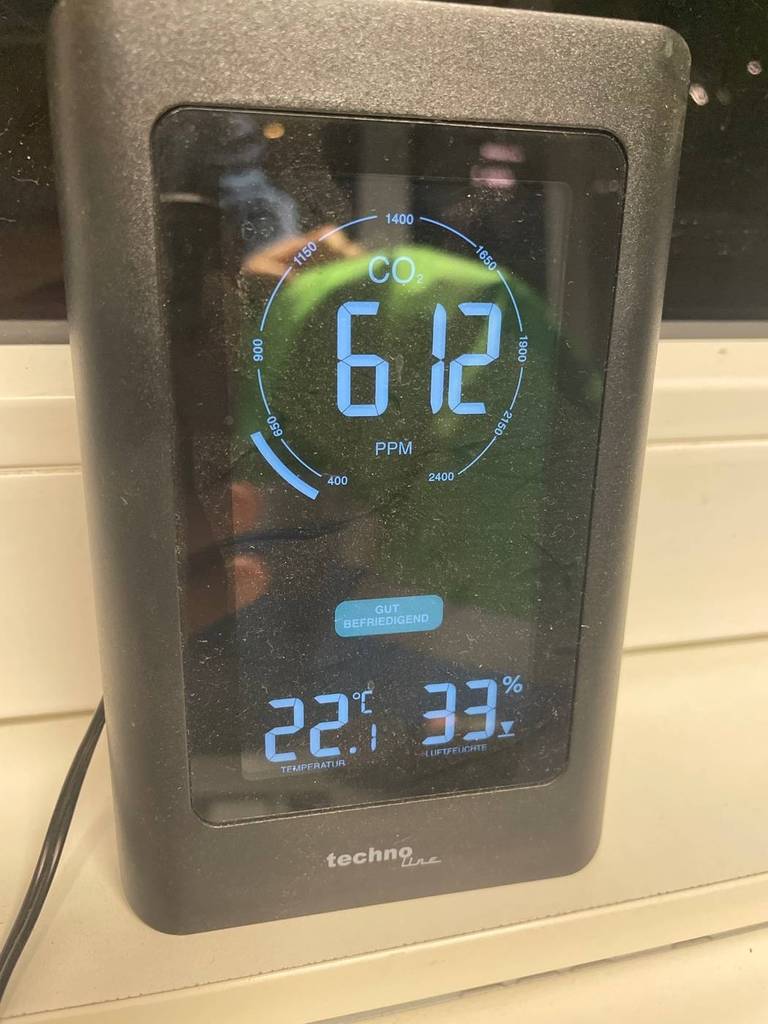 Nahaufnahme eines elektrischen, getesteten CO2-Melders in grauem Design mit eingeschaltetem Display an einem Fenster.