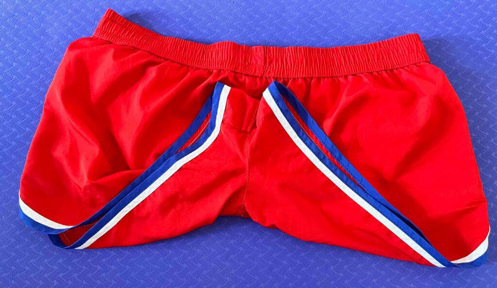 Eine rote getestete Badehose mit Zierstreifen, mit Fokus auf den schmalen Schritt, befindet sich auf einer blauen Oberfläche.
