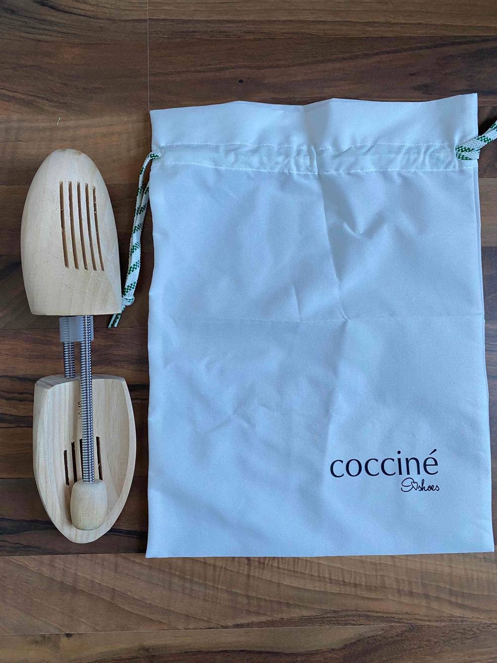 cocciné Stiefelspanner im Test befinden sich neben einem weißen Aufbewahrungsbeutel aus Stoff auf einem Holzboden.