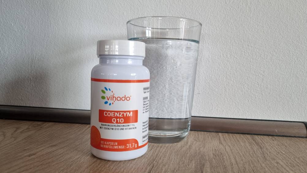 Coenzym Q10 Verpackung steht vor einem Glas Wasser