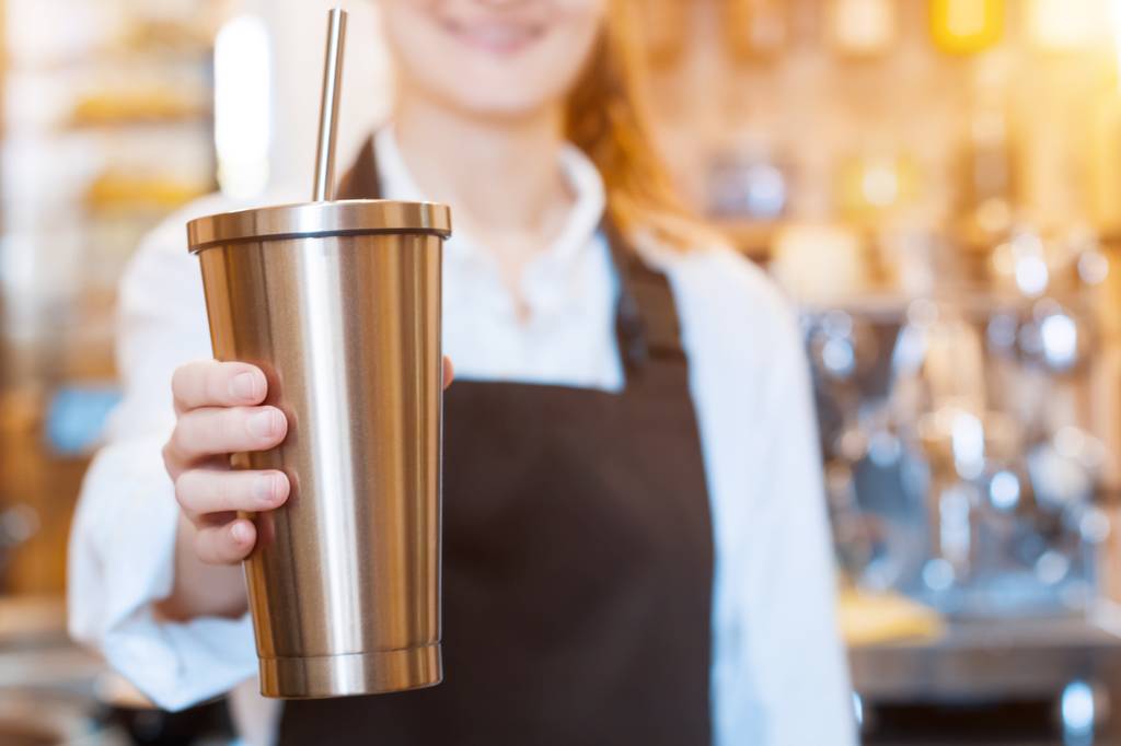 Coffee-to-go-Becher-Test: Ein Frau hält einen Coffee-to-go-Becher aus Edelstahl mit Strohhalm in der Hand. 