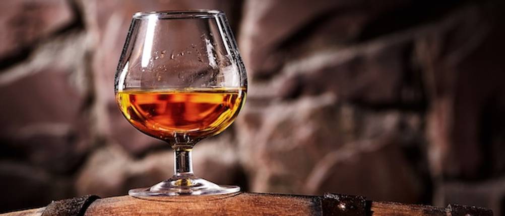 Cognacgläser im Test: Ein Cognacglas mit Cognac in Nahaufnahme auf einem Holzfass.