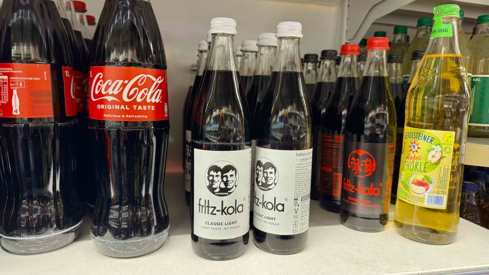 Mehrere Flaschen der Cola im Test in einem Verkaufsregal.