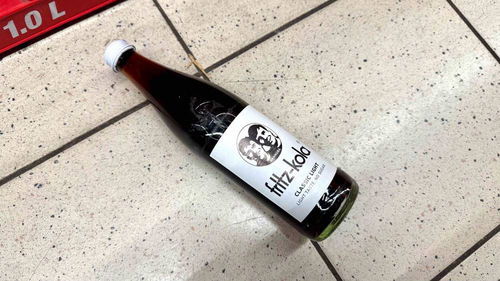 Eine Flasche der getesteten Cola liegt auf einem Fließenboden.