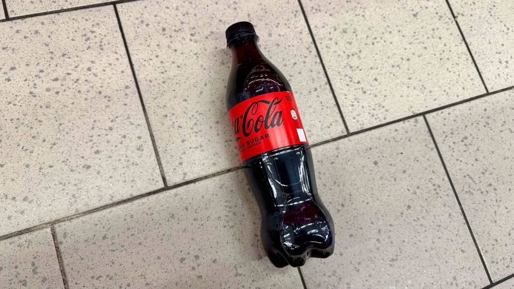 Eine Flasche Cola ohne Zucker im Test von schräg oben auf einem Fließenboden liegend.