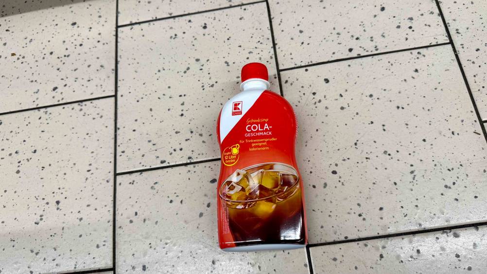 Eine Flasche des getesteten Cola-Sirups auf einem hellen Boden liegend.