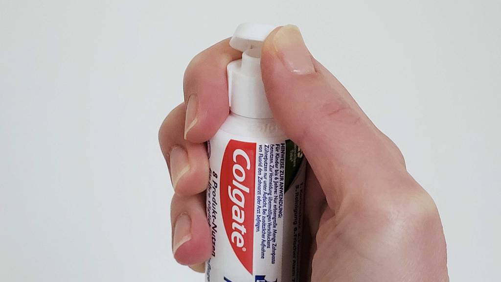 Eine Hand öffnet eine Tube Colgate-Zahnpasta zum Testen.