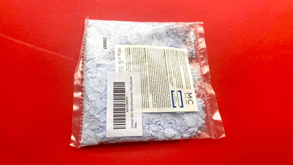 Ein getestetes Blondierpulver liegt in einer transparenten 100-g-Kunststofftüte auf einer roten Fläche.
