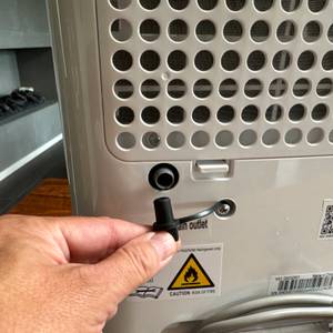 Eine Hand entfernt einen Stöpsel von der Rückseite des Comfee MDDF-20DEN7-WF