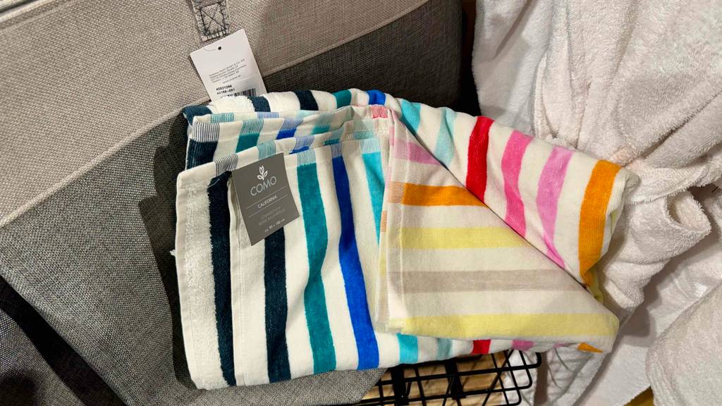 Getestet: Ein Strandtuch in bunt gestreiftem Design liegt neben einem weißen Bademantel.