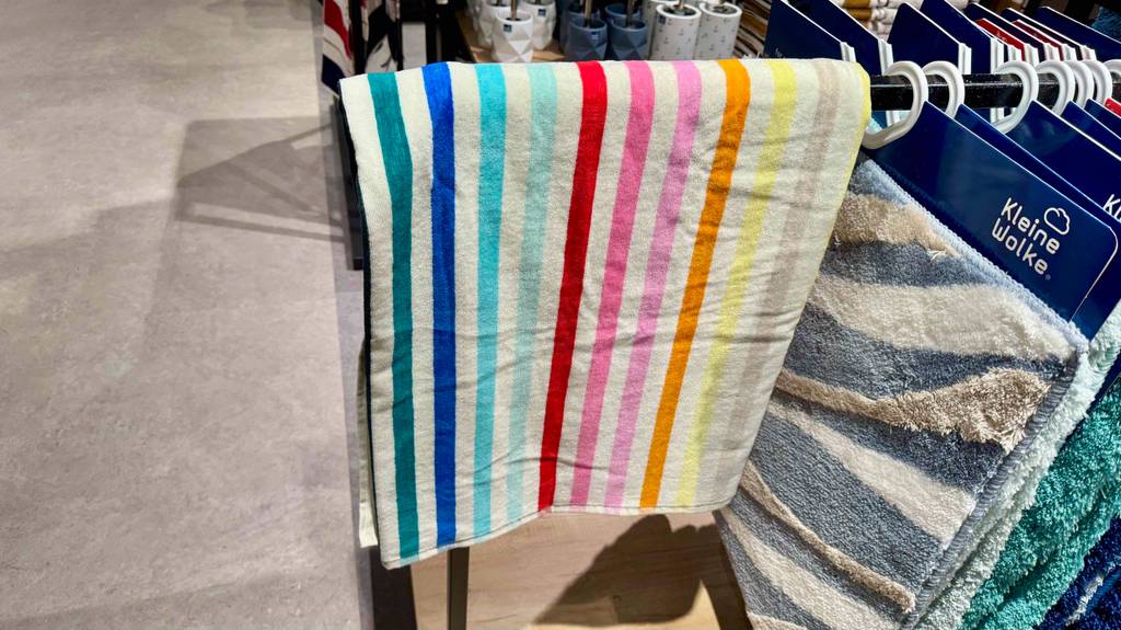 Im Test: Ein Strandtuch in bunt gestreiftem Design hängt über einer Stange neben den Badvorlegern.