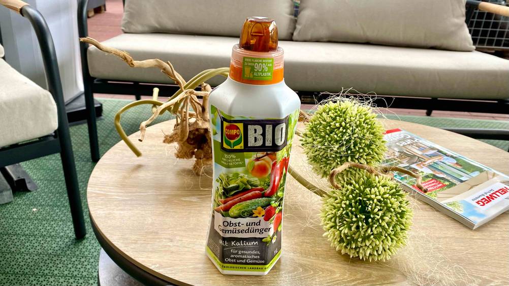 Im Test: Eine Flasche Obstbaum-Dünger steht auf einem Tisch mit Deko im Hintergrund eine Outdoorsofa.