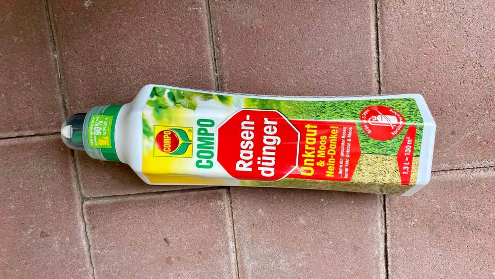 Eine Flasche des getesteten Rasendüngers gegen Unkraut liegt horizontal auf einem Steinboden.