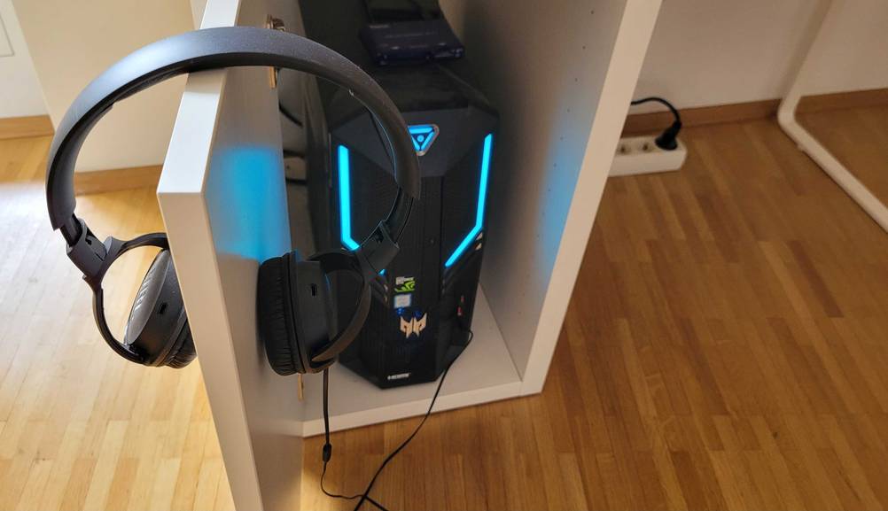 Computertisch im Test: An der geöffneten Türe hängen Kopfhörer, im Hintergund der Computer.