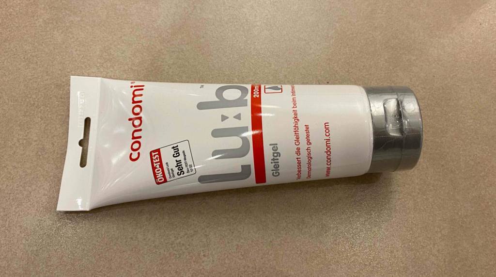 Eine weiße Tube Condomi Gleitgel im Test liegt auf einem beigefarbenen Untergrund.
