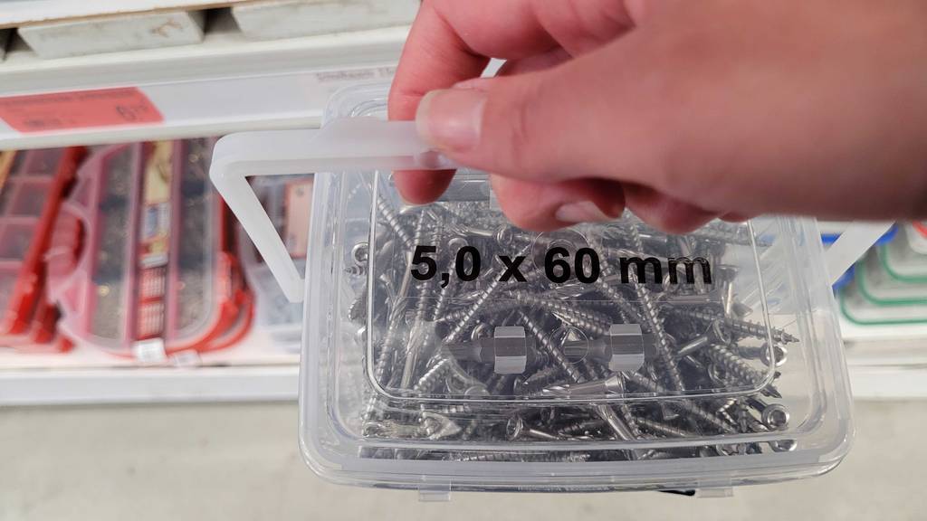 Im Test: Eine Hand hält eine Box mit Terrassenschrauben am Henkel.