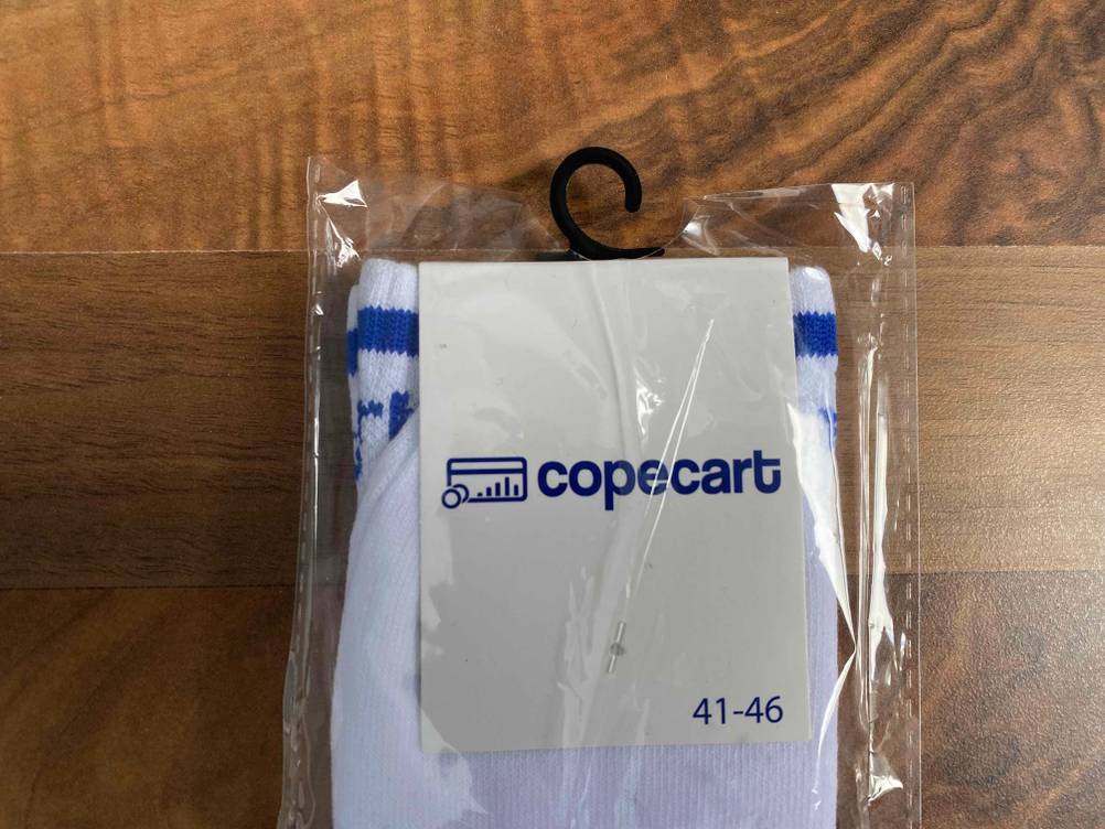 Weiße Copecart Tennissocken im Test liegen in ihrer Originalverpackung auf einem Holzboden.