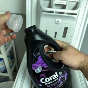 Die Verschlusskappe des Waschmittels für schwarze Wäsche von Coral wird abgehoben.