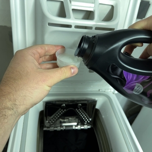 Die Verschlusskappe des Waschmittels für schwarze Wäsche von Coral wird mit Waschmittel gefüllt.