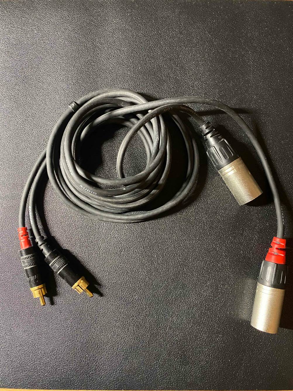 Ein getestetes Cinch-Kabel zusammengerollt auf einer dunklen Fläche.