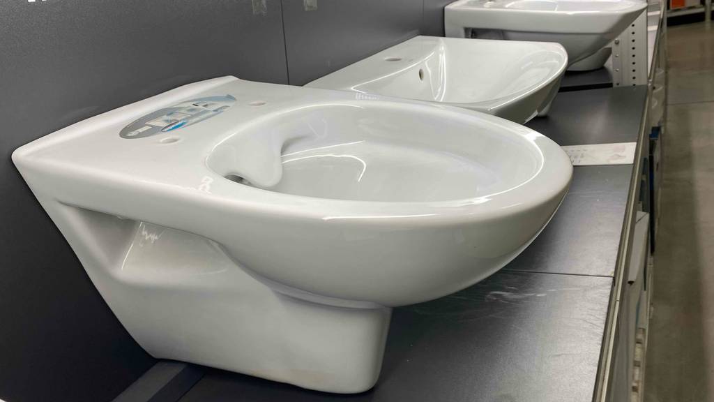 Ein weißes getestetes Wand-WC befindet sich montiert neben weiteren weißen Sanitär-Produkten im grauen Ausstellungsbereich eines Geschäfts.
