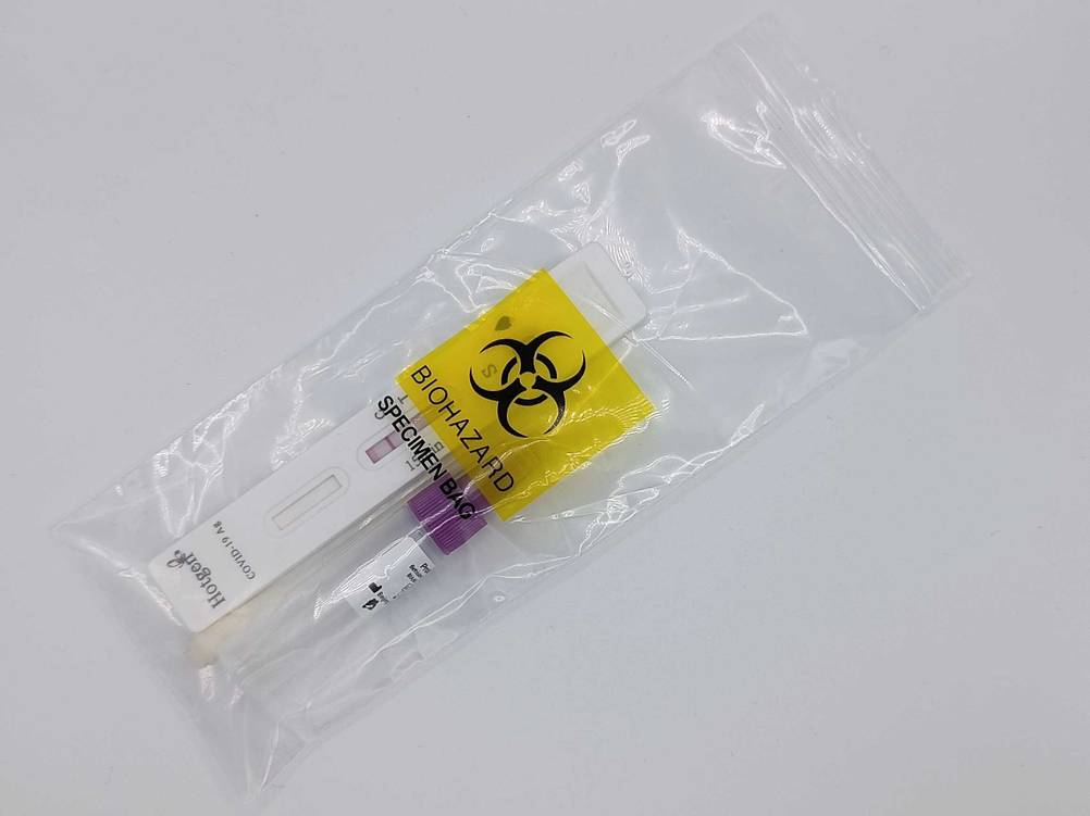 Eine transparente Tüte mit Biohazard-Aufdrück beim Hotgen-Corona-Schnelltest, in der sich der Teststreifen und eine Fläschchen befindet.