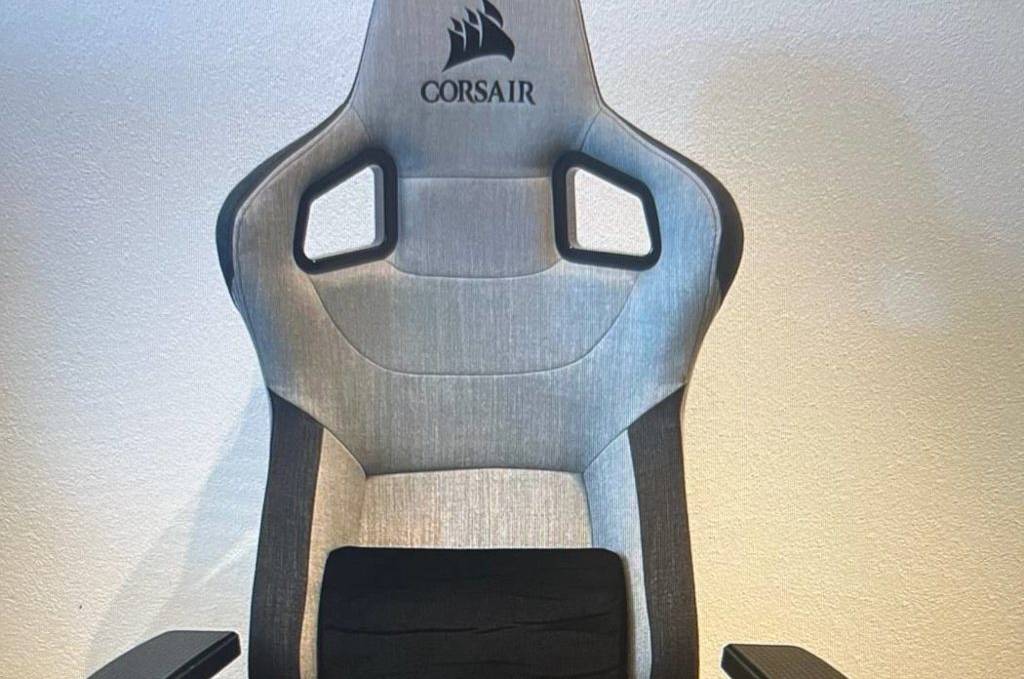 Vorderansicht eines hellgrauen, mit schwarzen Elementen abgesetzten Bezugs eines Corsair T3 Rush Bürostuhl im Test, der auf einem Holzboden vor weißer Wand steht.