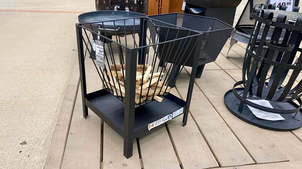 Feuerschalen im Test: Seitenansicht auf mehrere schwarze Feuerschalen, im Vordergrund steht ein viereckiges Corvo Modell, inklusive kleiner Holzstückchen, auf Holzlatten in einem Verkaufsbereich.