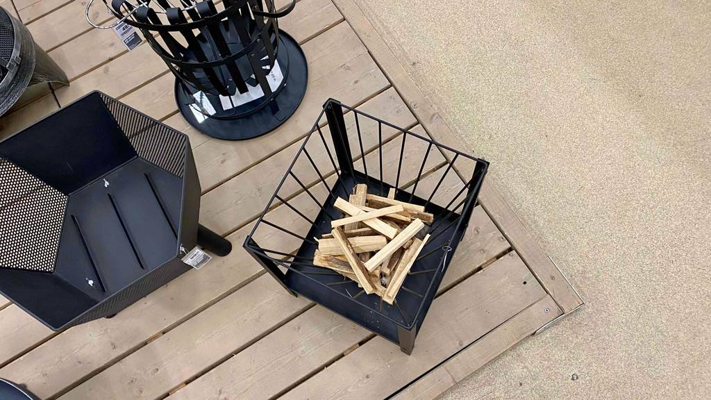 Feuerschalen-Test: Ansicht von oben auf mehrere schwarze Feuerschalen inklusive eines viereckigen Corvo Modells mit Holzstückchen auf einem Holzboden im Verkaufsbereich.