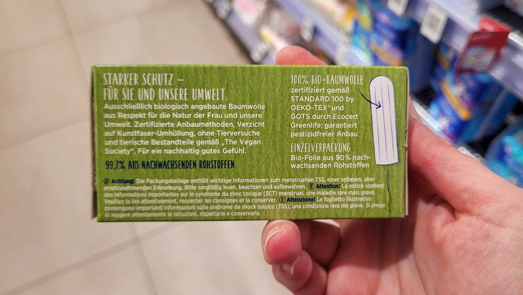 Bio-Tampons im Test: Eine Hand hält eine grüne Verpackung, auf der Produkthinweise gedruckt sind.