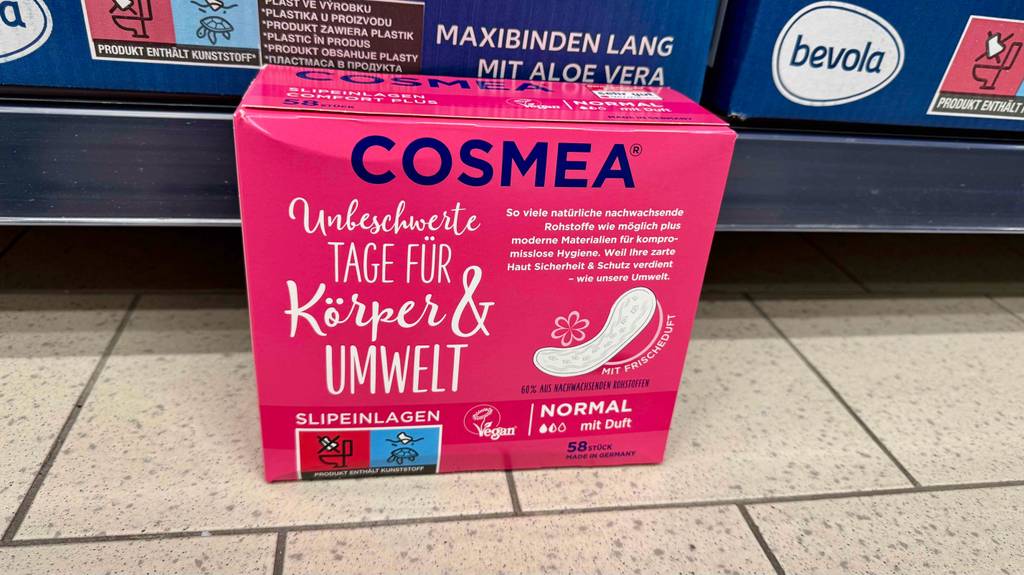Getestete Cosmea-Slipeinlagen in der rosafarbenen 58-Stück-Verpackung stehen vor einem Verkaufsregal auf dem Boden.
