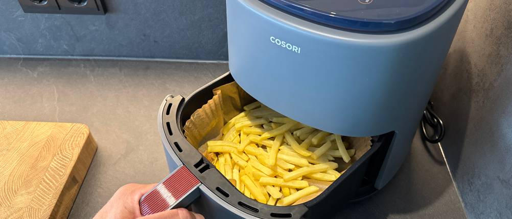 Eine Hand schiebt den mit Pommes gefüllten Behälter in die Cosori CAF-LI401S.
