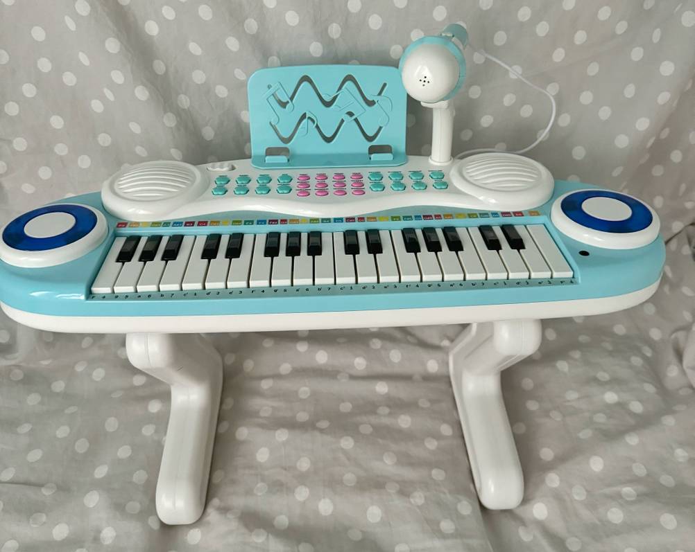 Kinderkeyboard-Test: Ein Modell im weiß-hellblauen Design inklusive Standfüßen und Mikrofon steht auf einer grau-weiß gepunkteten Bettdecke.