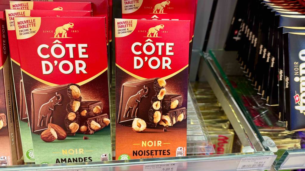 Eine getestete Côte d’Or-Schokolade in der roten Verpackung mit Nüssen steht in einem Verkaufsregal neben diversen Schokoladensorten.