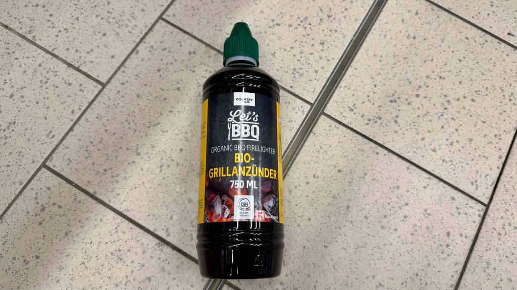 Eine Flasche getesteter flüssiger Grillanzünder liegt auf einem hellen Fliesenboden.