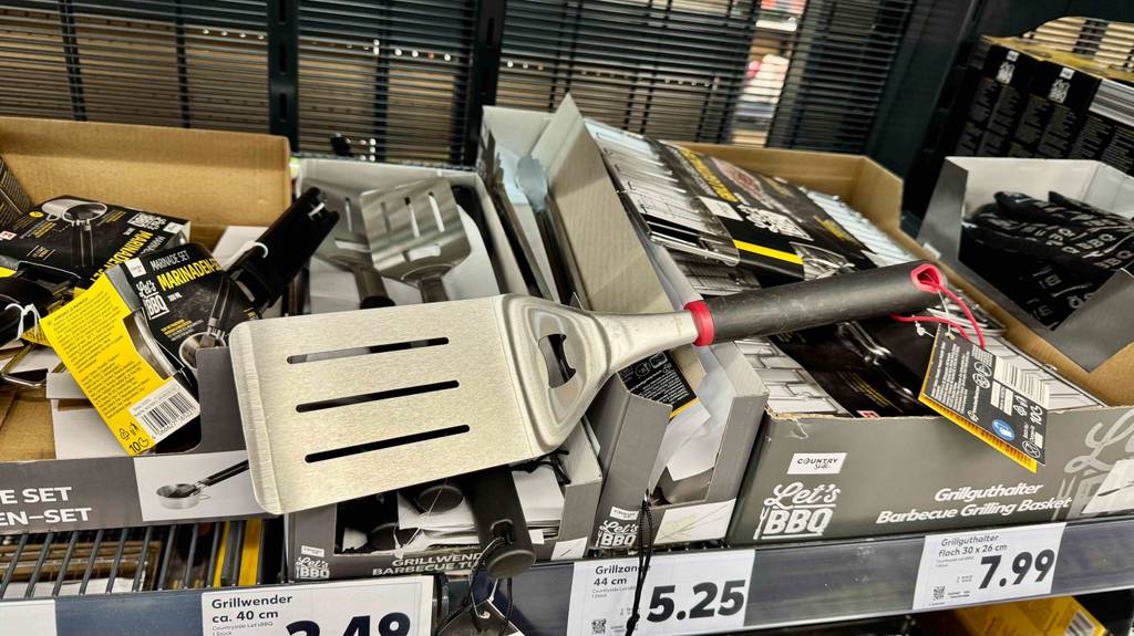 Grillwender-Test: Ein Modell mit schwarzem Kunststoffgriff inklusive Öse zum Aufhängen liegt auf einem Verkaufsregal über Grillguthaltern.