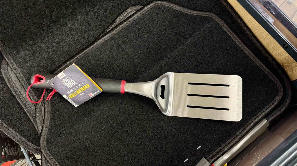 Getestet: Ein Grillwenderinklusive schwarzem Kunststoffgriff mit Öse zum Aufhängen liegt auf einer schwarzen Matte.