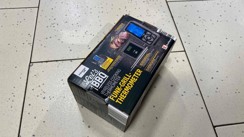 Ein Funk-Grillthermometer im Test befindet sich in seiner schwarzen Verpackung auf einem weißen Fliesenboden.