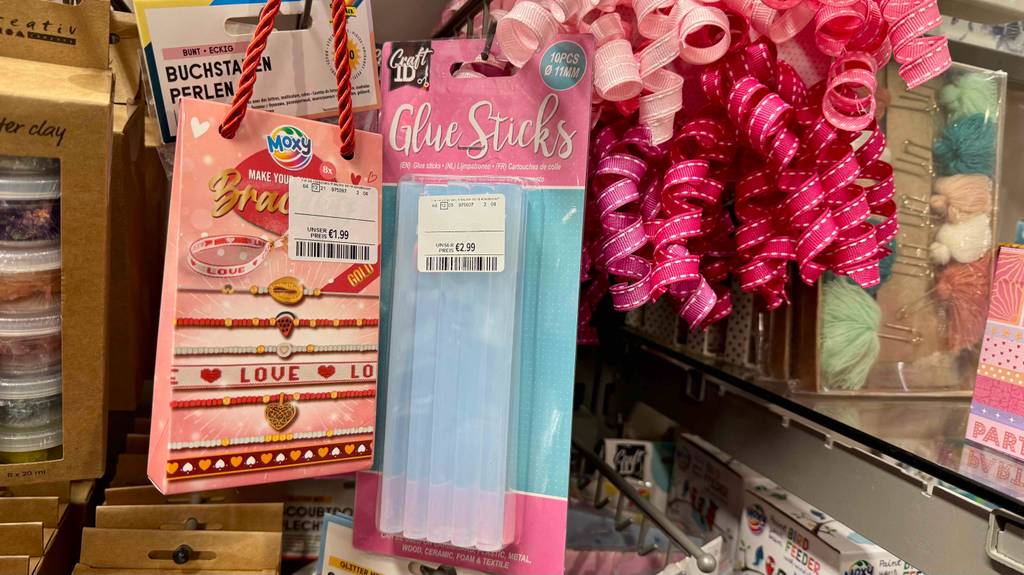 Getestete Heißklebesticks in der 10-er-Packung hängen an einem Verkaufsstand neben weiterem Bastelzubehör.