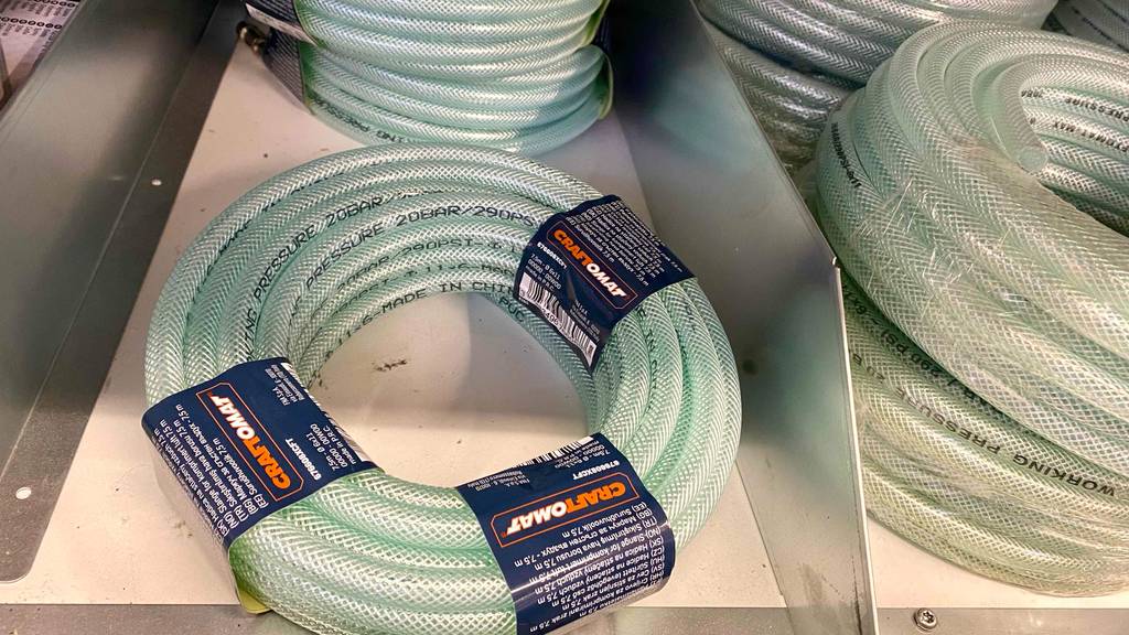 Druckluftschläuche im Test: mehrere verstärkte Druckluftschläuche inklusive Schnellkupplung liegen neben- und übereinander auf einem weißen Regal im Verkauf.