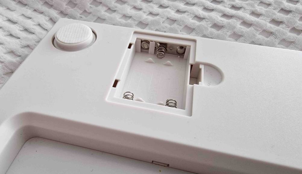 Detailansicht von oben auf das geöffnete Batteriefach einer weißen, getesteten Körperfettwaage.