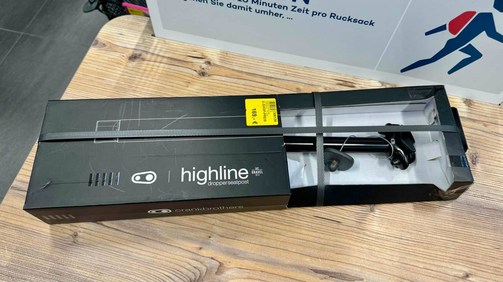 Eine verpackte absenkbare Sattelstütze liegt zum Testen auf einer Holzfläche.
