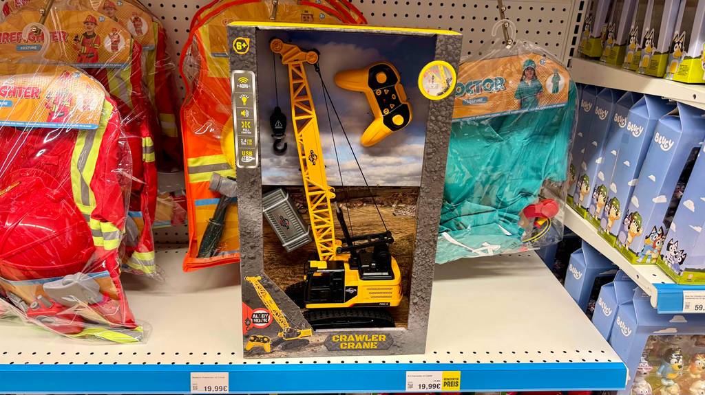 Auf einem Regal mit in Zellophan verpackter Kinderverkleidung steht der getestete Spielzeug-Kran in der Verpackung.