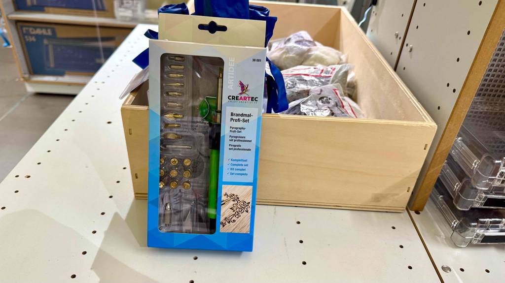 Das getestete Brandmalerei-Set von Creartec befindet sich in seiner Verpackung vor einer Holzkiste im Baumarkt.
