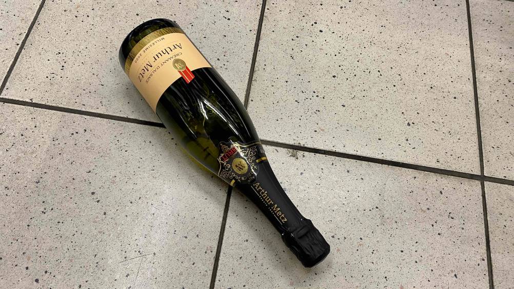 Nahaufnahme des Flaschenkopfes eines getesteten Crémant d’Alsace auf einem Fließenboden.