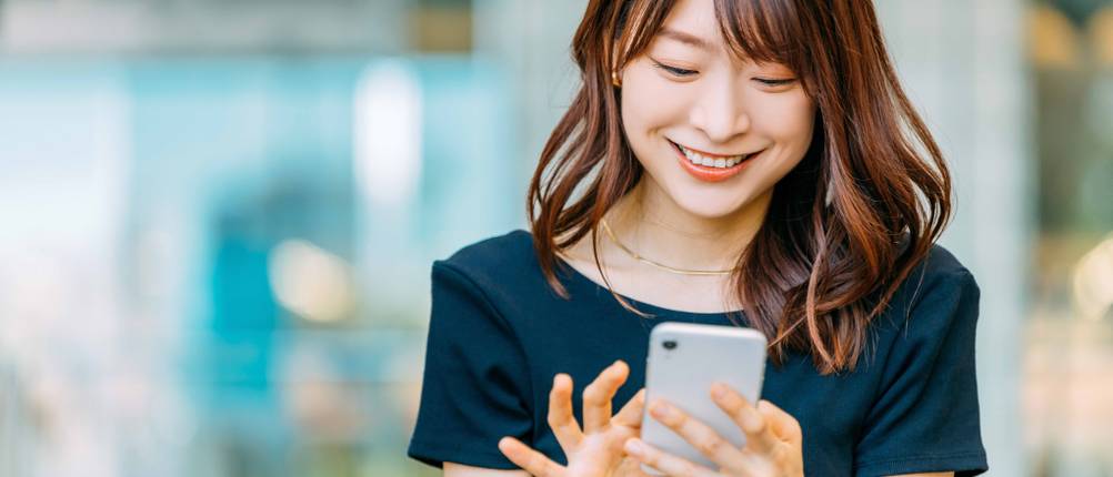 CRM-Software im Test: Frau lächelt während sie am Smartphone ist.