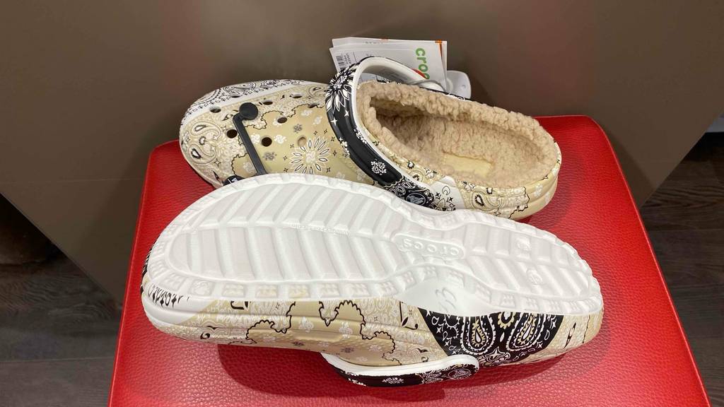 Crocs getestet: Ein Schuh liegt mit der Sohle nach oben neben vor einem stehenden auf roter Fläche.