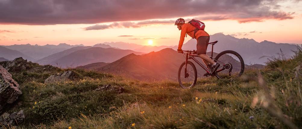 Klickpedalen im Test: Ein Cross-Country-Fahrradfahrer fährt in einem bergigen Gelände auf einer hügeligen Wiese.
