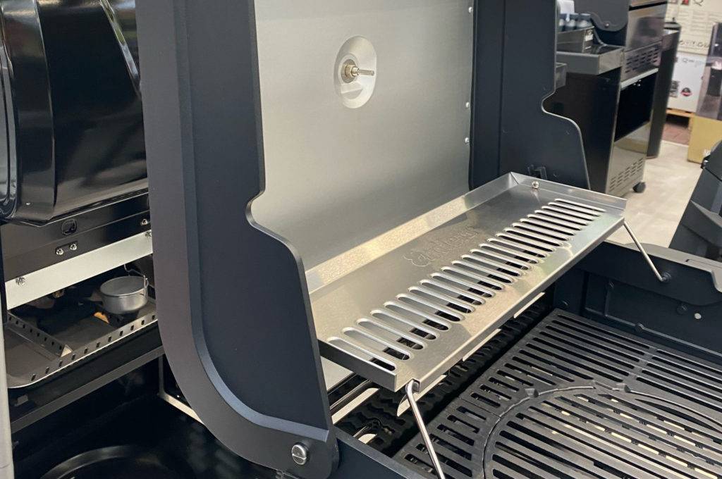 Im Test: geöffneter Gasgrill mit Seitenbrenner der Marke Cubiq, mit Fokus auf die Abdeckung und den Grillrost.