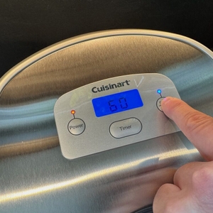 Eine Hand drückt einen Knopf auf der Cuisinart ICE100E.